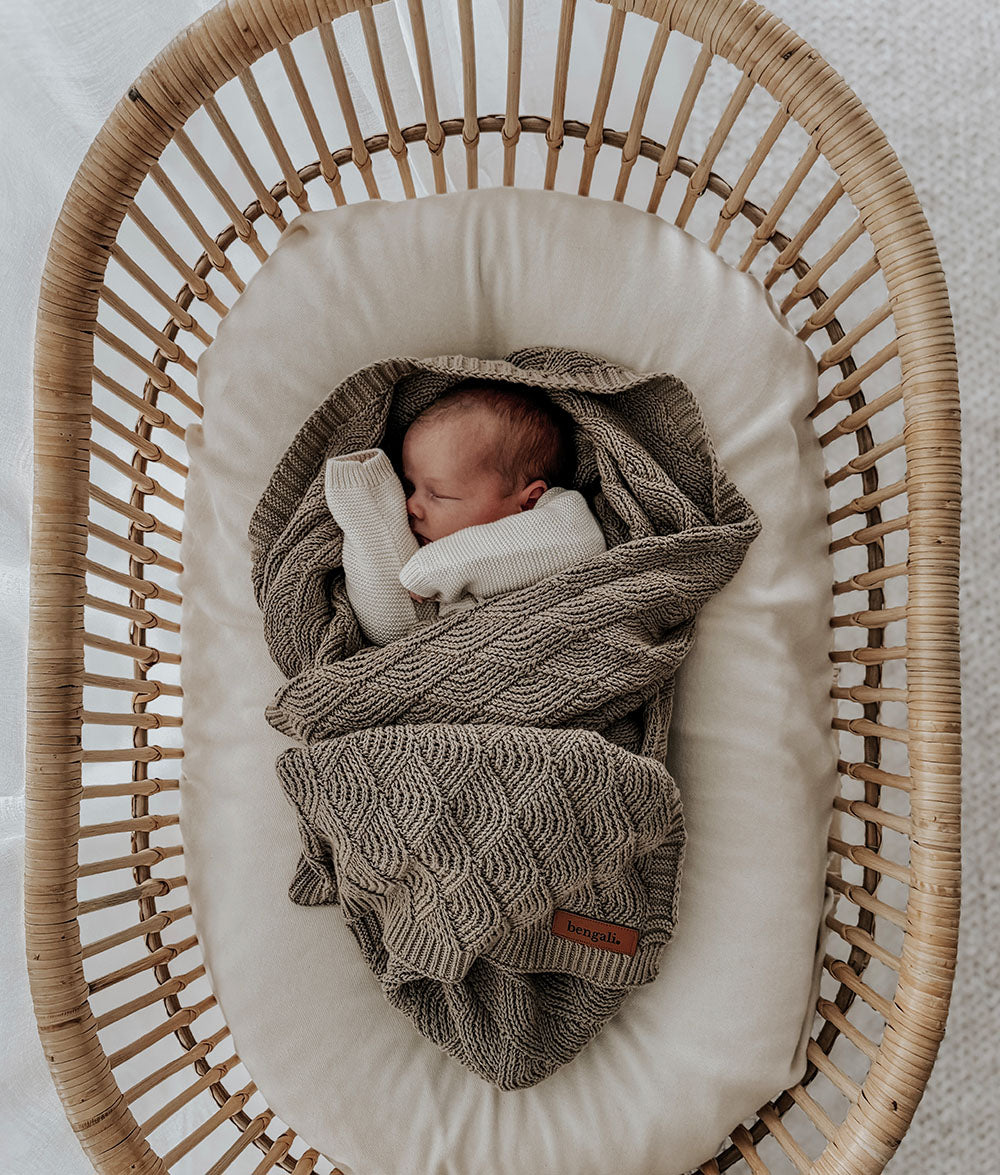 Newborn baby wrapped in a stone blanket in a wicker crib with a neutral background
