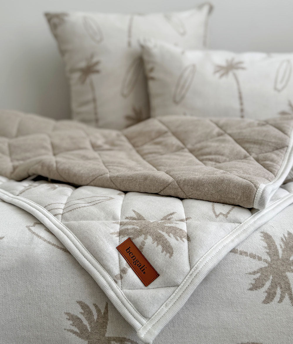 Quilted blanket with palm tree pattern on a bed with matching pillows.