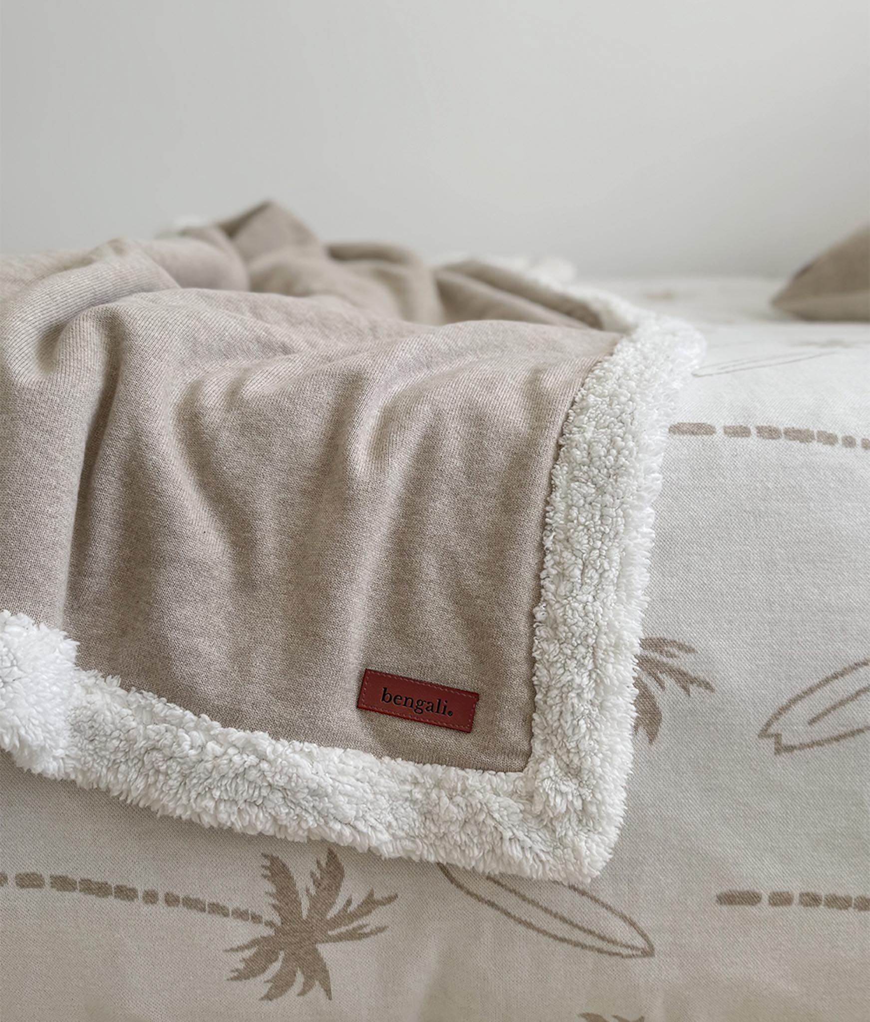 Beige blanket with white sherpa lining and a brand label on a neutral background