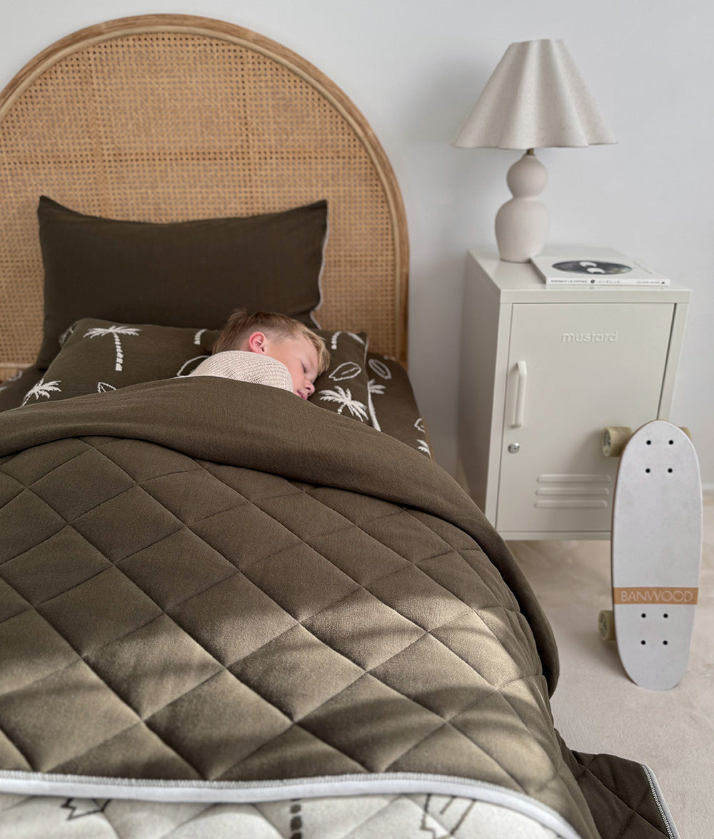 Child sleeping in Olive Surfing Palm jersey cotton bedding.