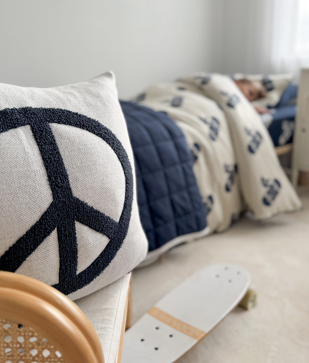 Peace cushion cover styled on a child's bed.