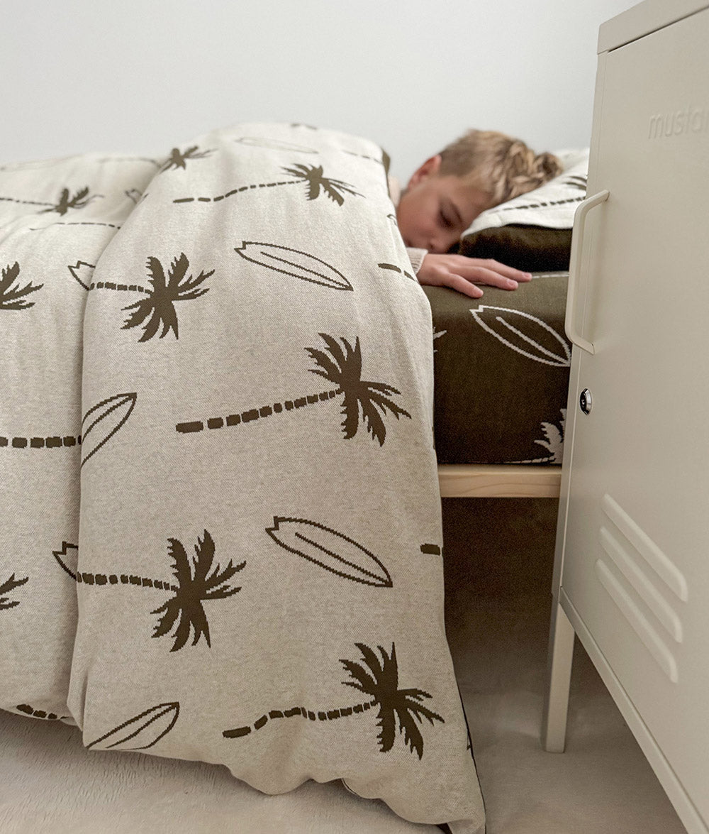 Child sleeping in Olive Surfing Palm bedding from bedside view.