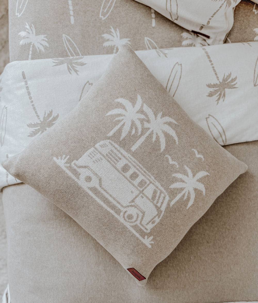 Beige pillow with white graphic of a van and palm trees on a beige surface.