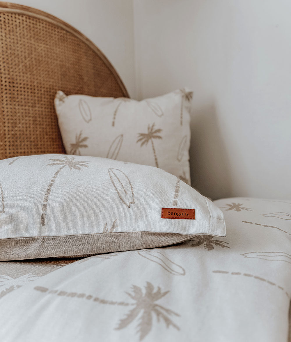 Palm tree patterned pillows on a bed with a wicker headboard.