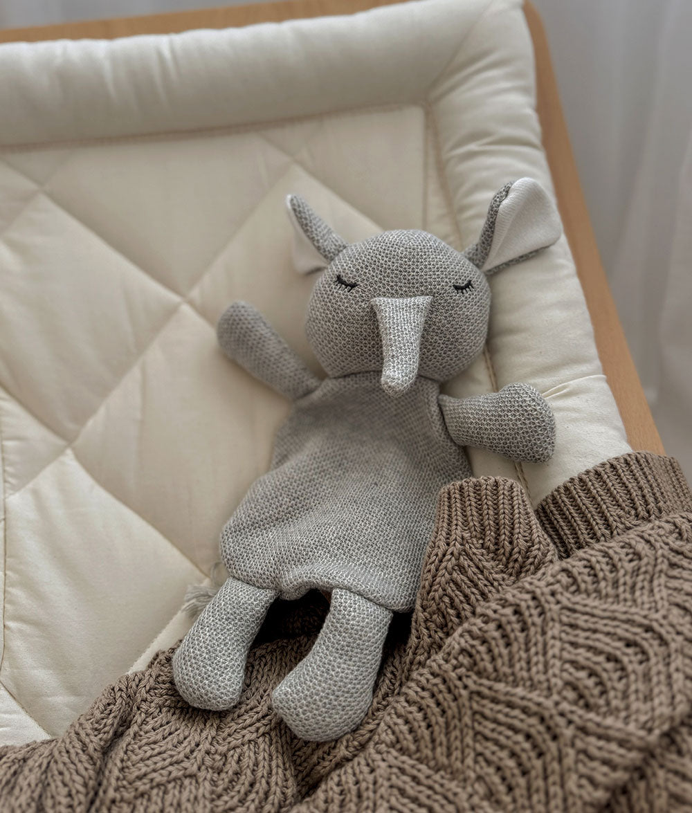 Gray knitted elephant toy on a quilted surface with a brown textured blanket
