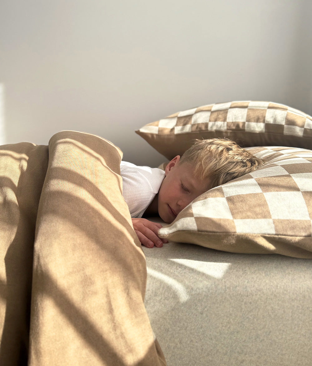 Child resting on the Khaki Gingham reversible pillowcase.