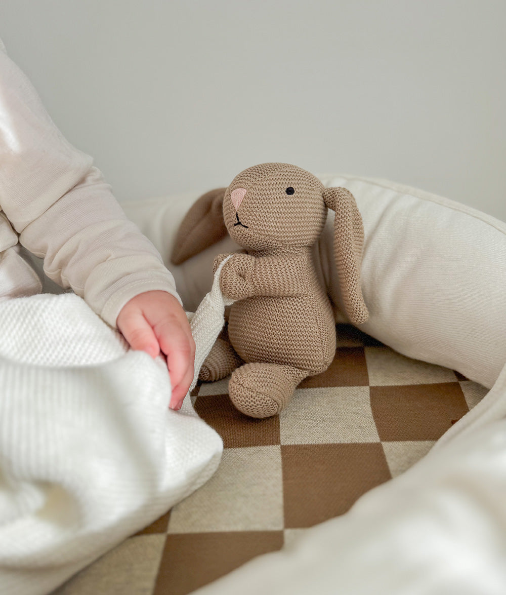 Knitted bunny toy styled in the baby lounger with khaki gingham mattress.